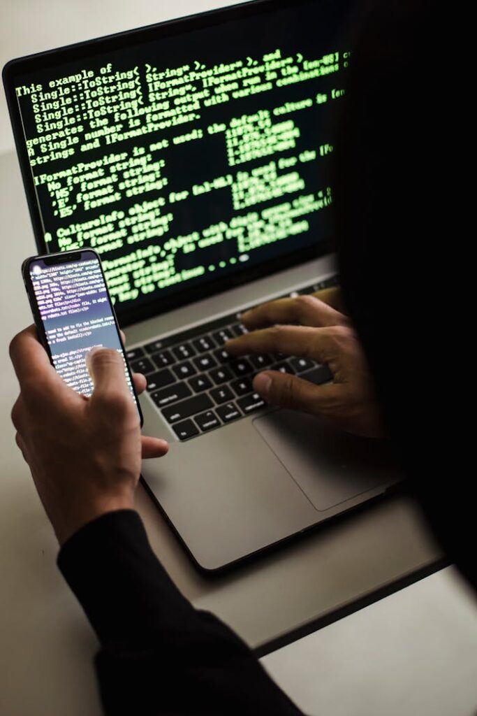 unrecognizable-hacker-with-smartphone-typing-on-laptop-at-desk-5935791 Unrecognizable hacker with smartphone typing on laptop at desk